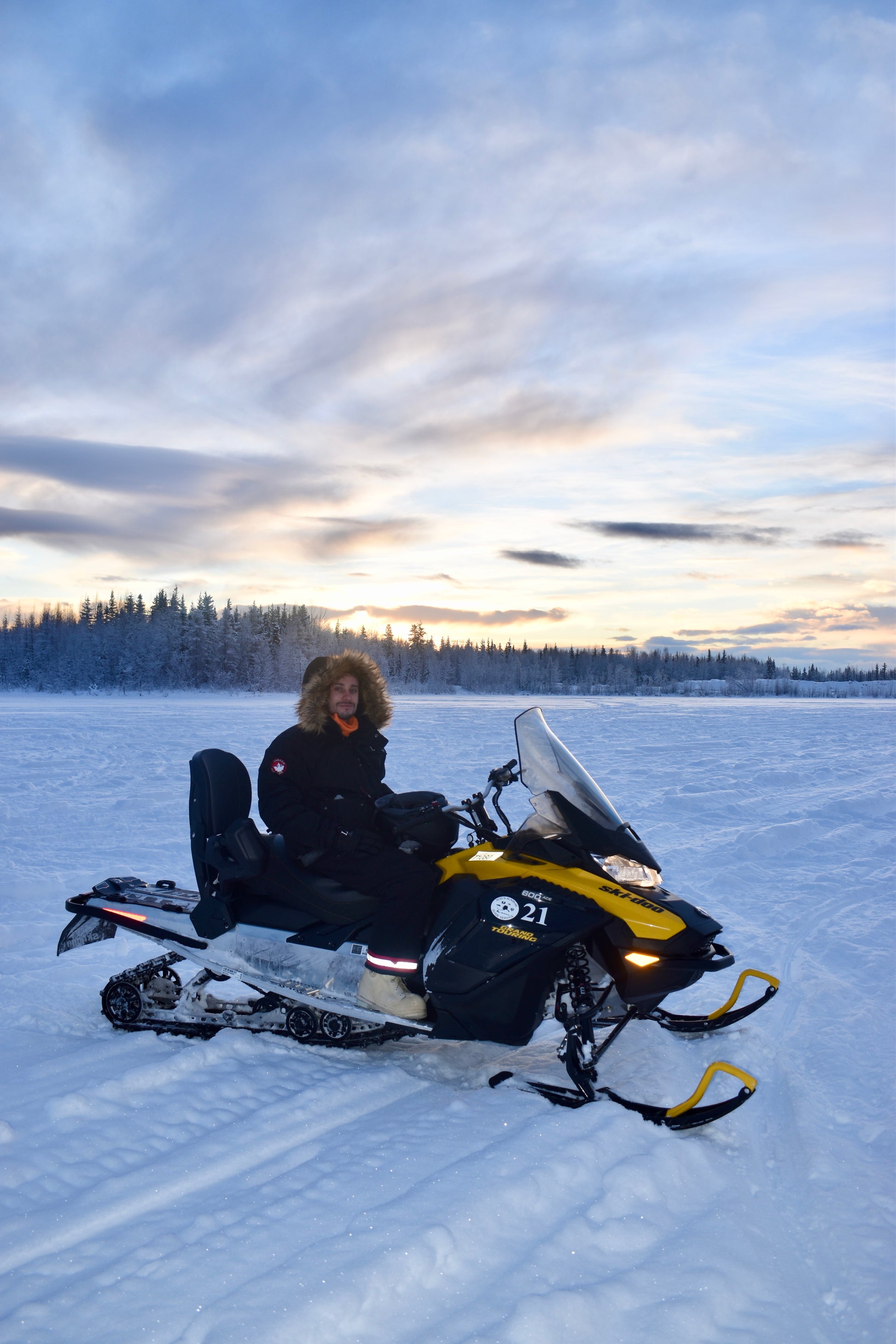 Person sitting on a snowmobile in a snowy landscape with a sunset sky.