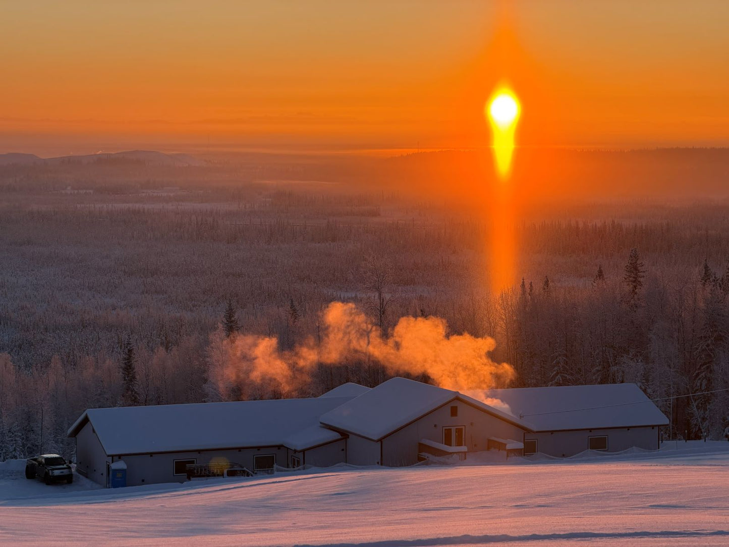 Sunset over a snowy landscape with houses and trees, glowing orange and yellow. Fairbanks Alaska 