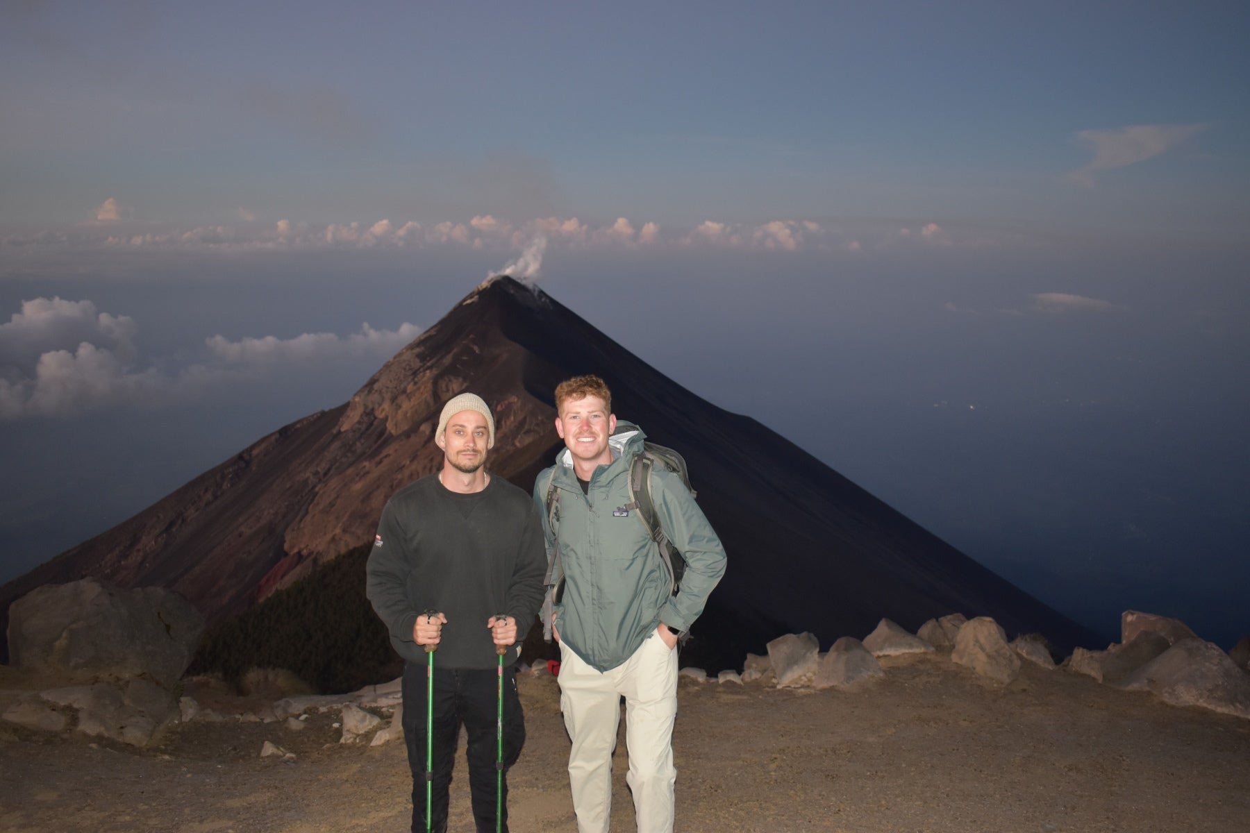 Two people standing on a mountain peak with a volcano in the background on acatenago in guatemala 